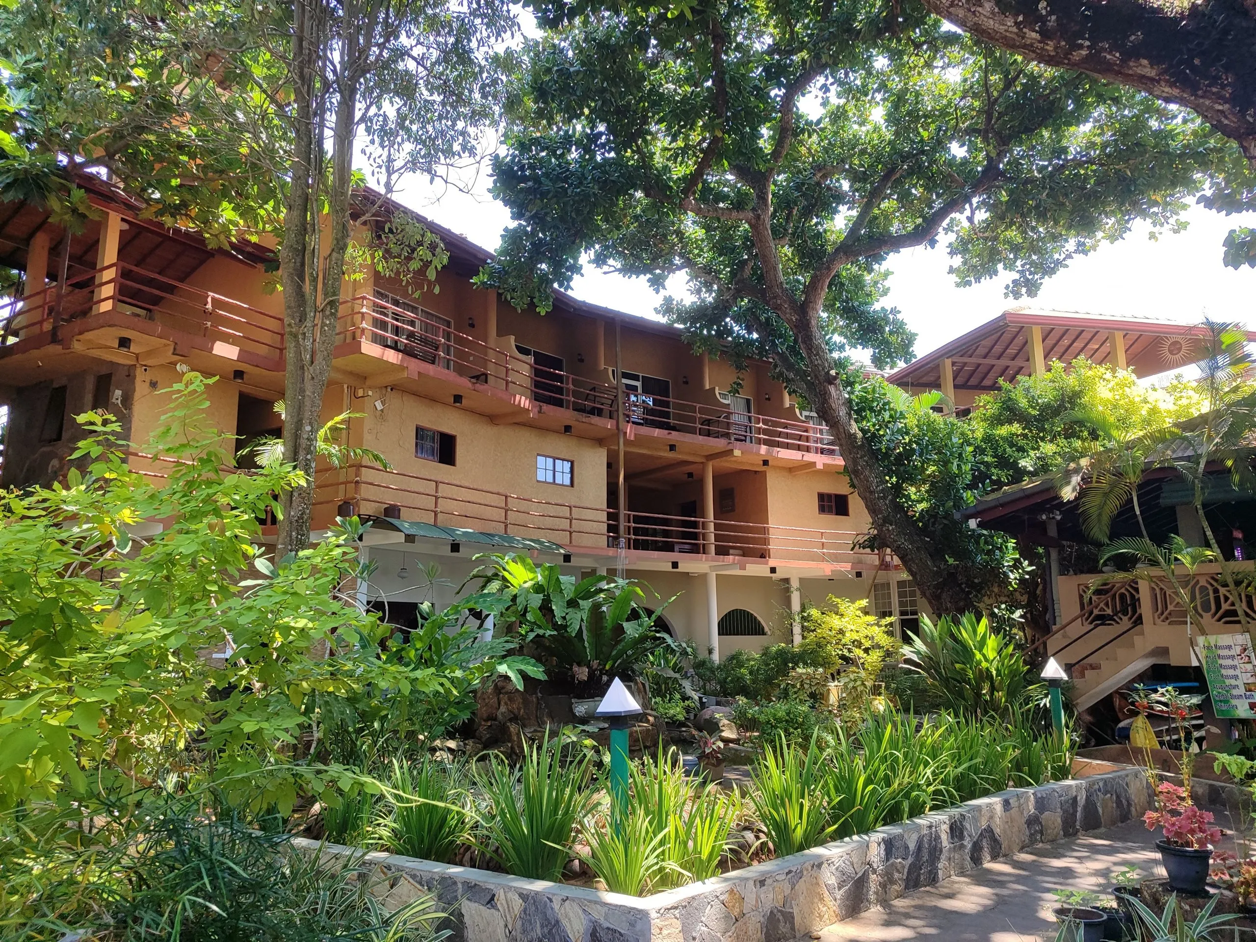 A low guesthouse building among trees and garden