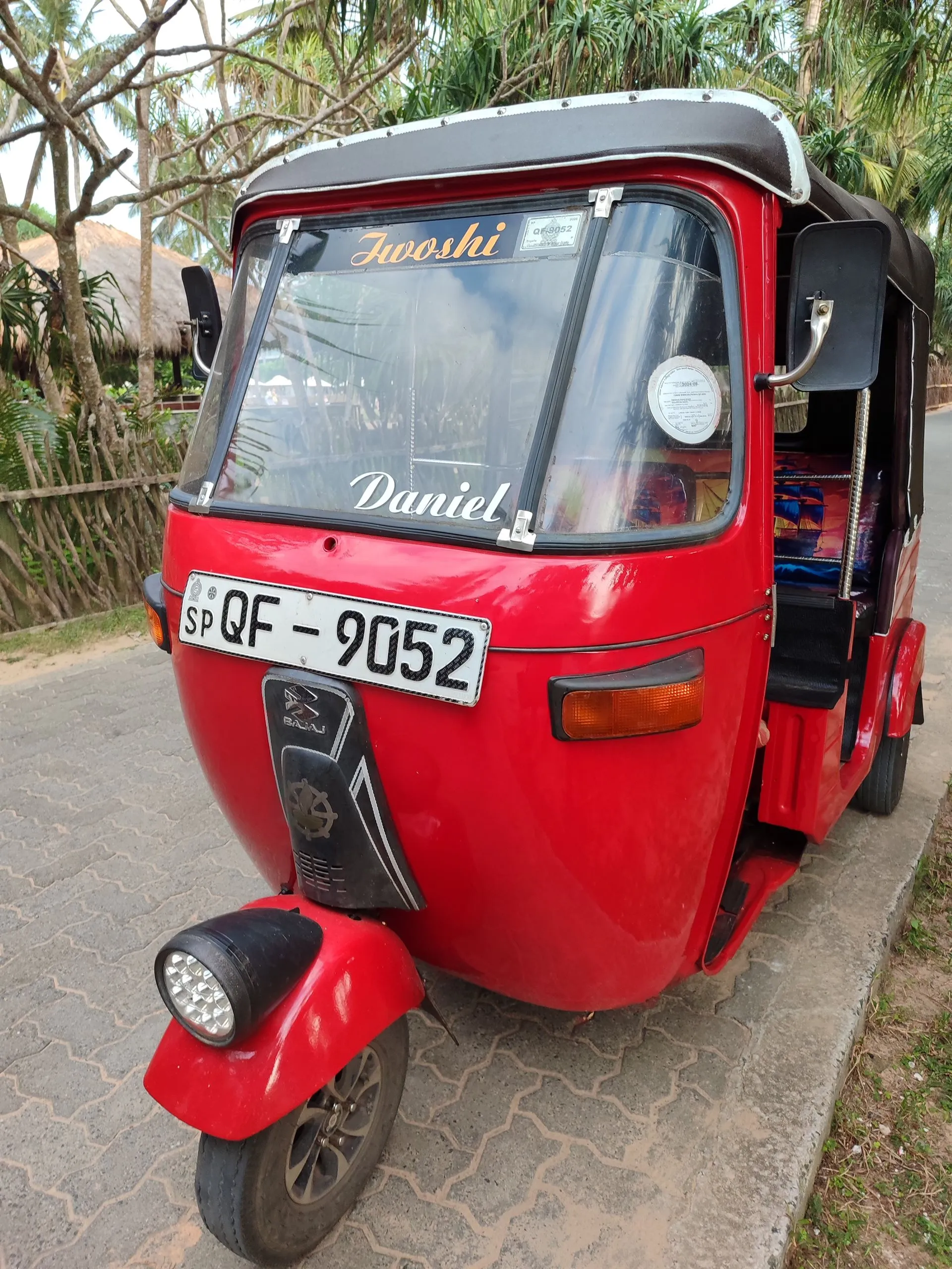 A red tuk-tuk with the driver's name painted across the windscreen