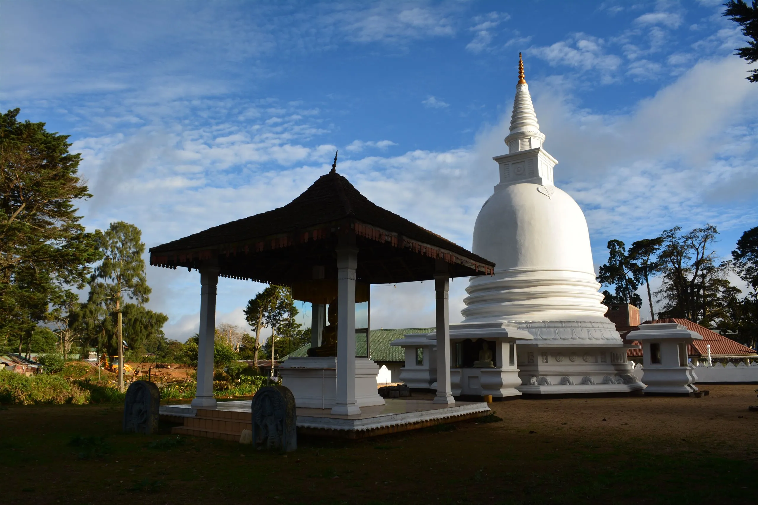 A white stupa and an open pavilion with a golden Buddha at a hill-country temple
