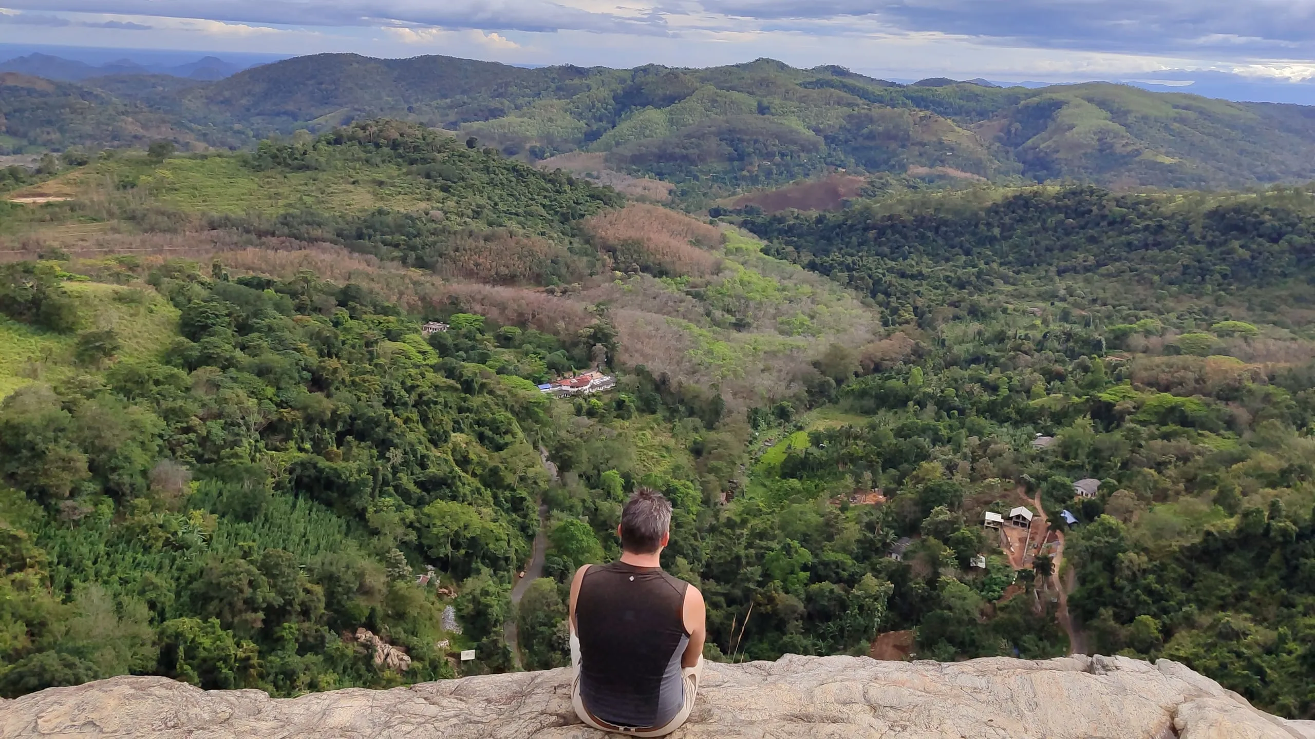 A guest sitting on a rock ledge above a wide valley of forested hills