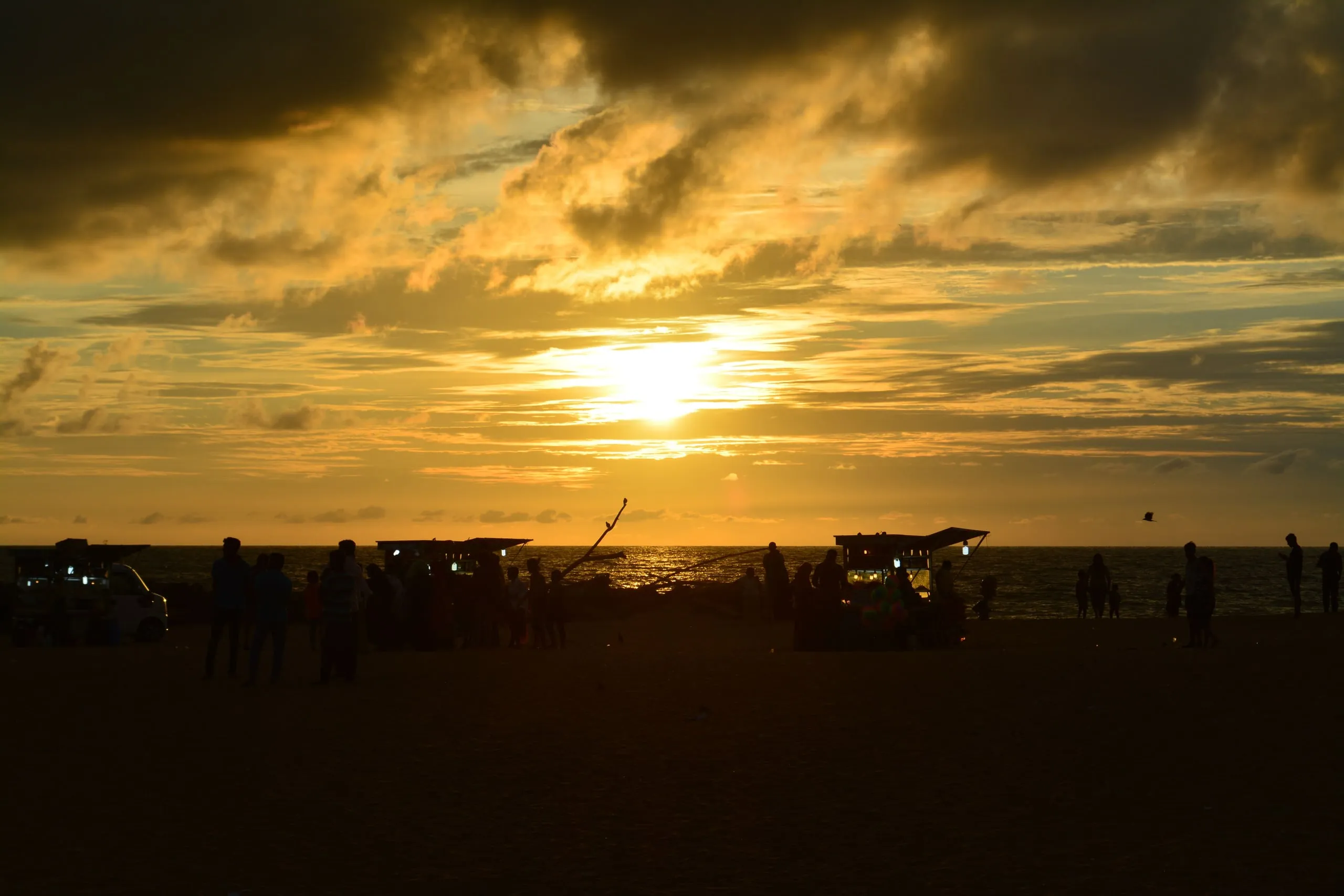 Sunset over the sea at Negombo beach, with people and food carts in silhouette along the shore