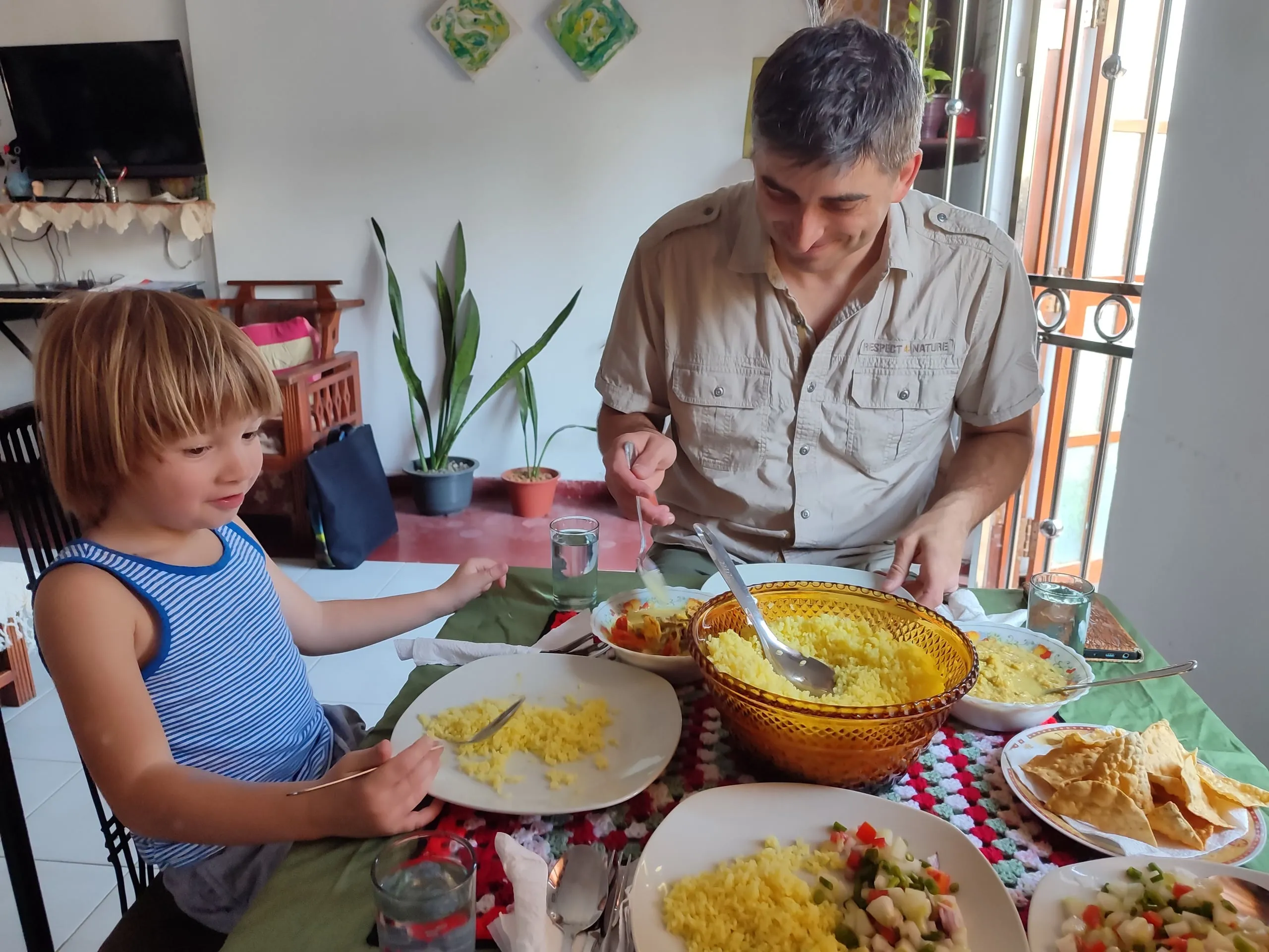 A man and a small boy at a family dining table with yellow rice, curries and papadums