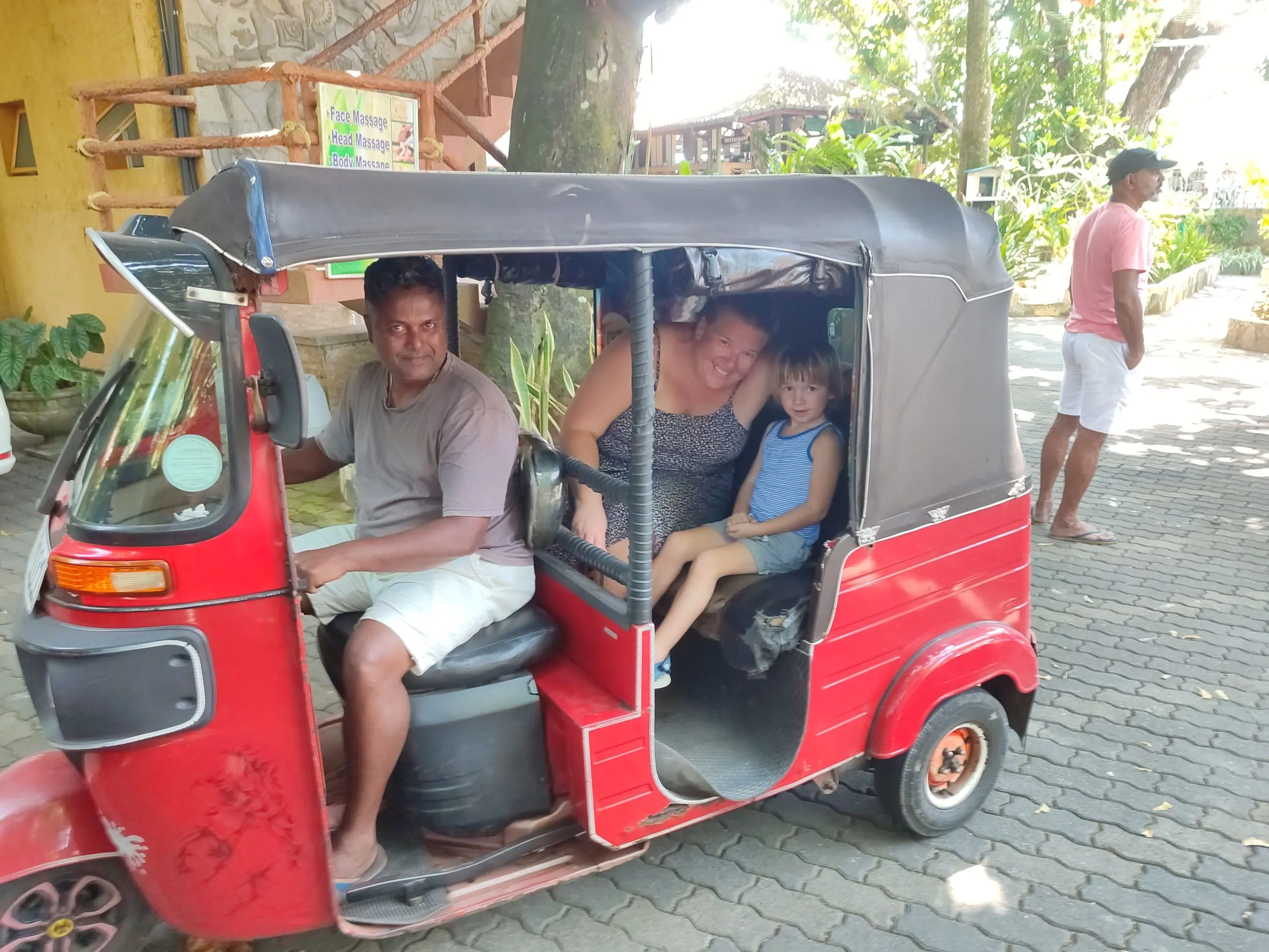A woman and a small boy sitting in the back of a red tuk-tuk with the driver at the wheel